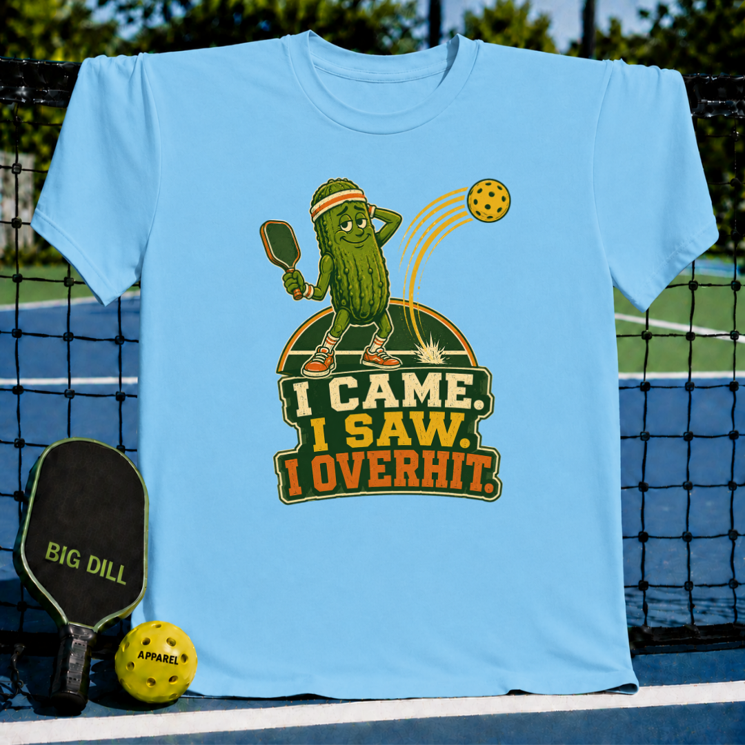 Light blue crew neck t-shirt featuring a cartoon pickle playing pickleball with the text I Came, I Saw, I Overhit.