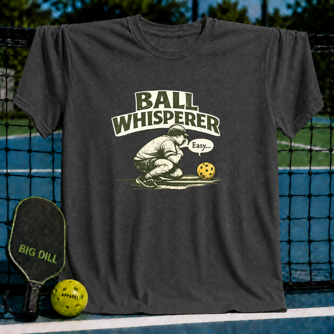 Charcoal grey unisex t-shirt featuring a vintage pickleball graphic with the text Ball Whisperer and a player crouching.