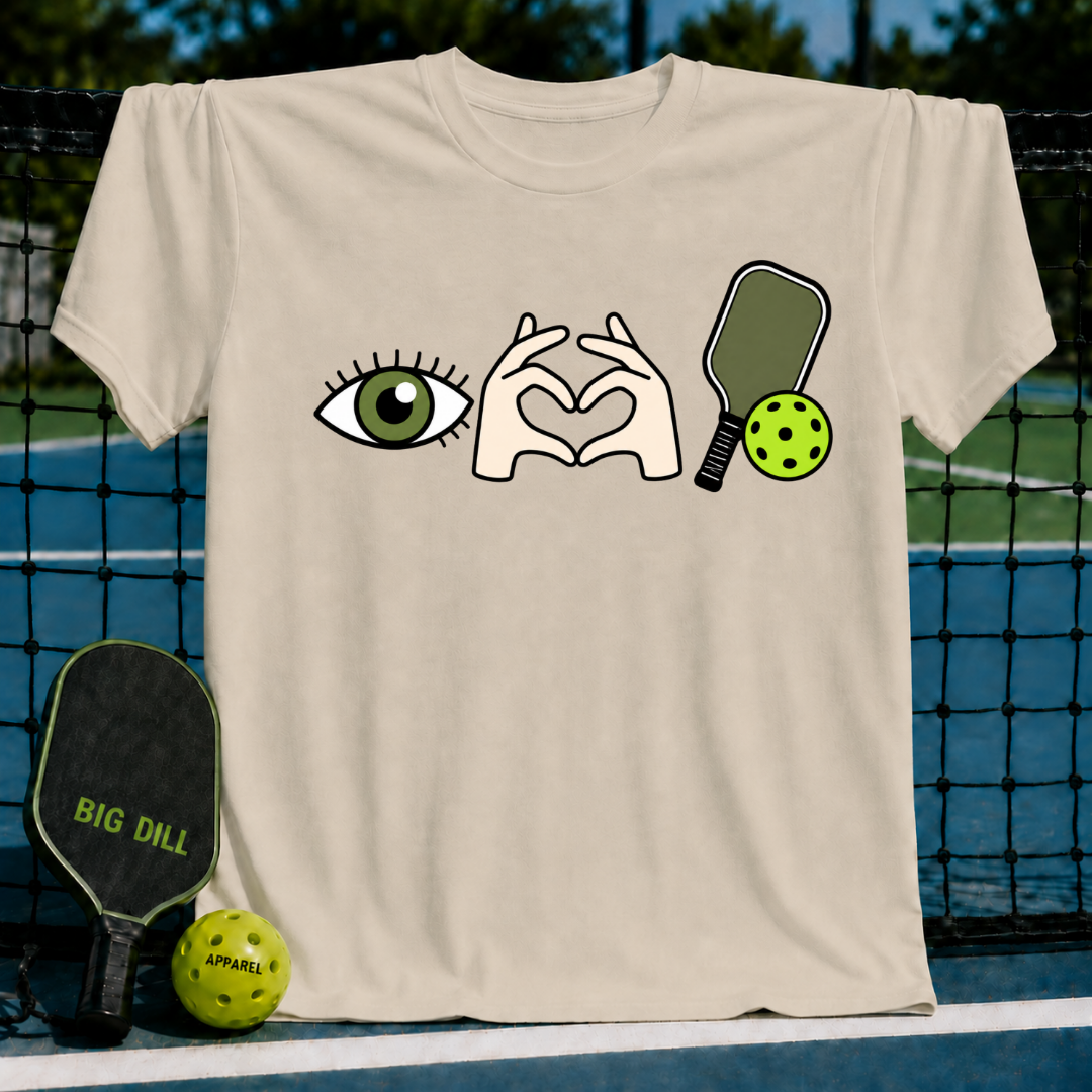 Beige cotton t-shirt featuring an eye, heart-shaped hands, and pickleball paddle graphic on a court background.