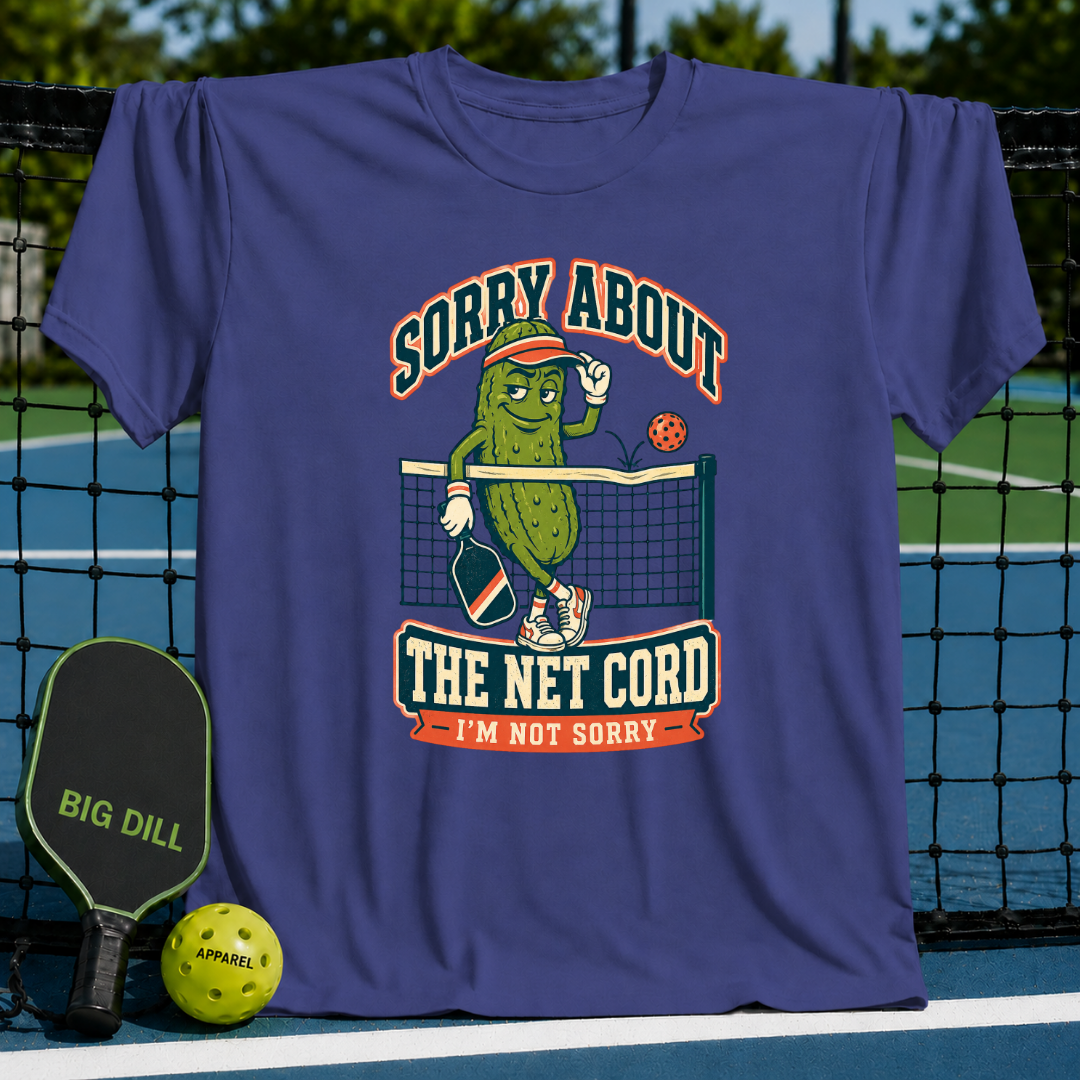 Purple crewneck t-shirt featuring a cartoon pickle playing pickleball with the text Sorry About The Net Cord.