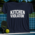 Navy blue unisex t-shirt featuring distressed white varsity lettering that reads Kitchen Violator, displayed on a pickleball court.