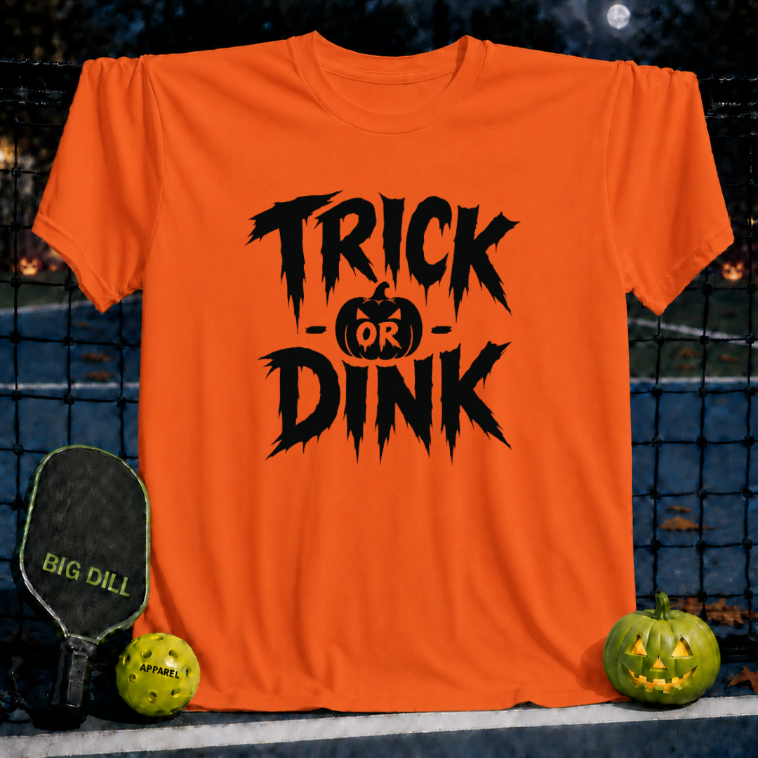Orange unisex T-shirt featuring a black Trick or Dink Halloween graphic with a pumpkin, displayed on a pickleball court.