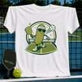 White cotton t-shirt featuring a cartoon pickle playing pickleball with a paddle and ball on a court graphic.