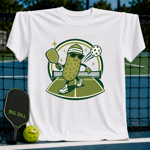 White cotton t-shirt featuring a cartoon pickle playing pickleball with a paddle and ball on a court graphic.