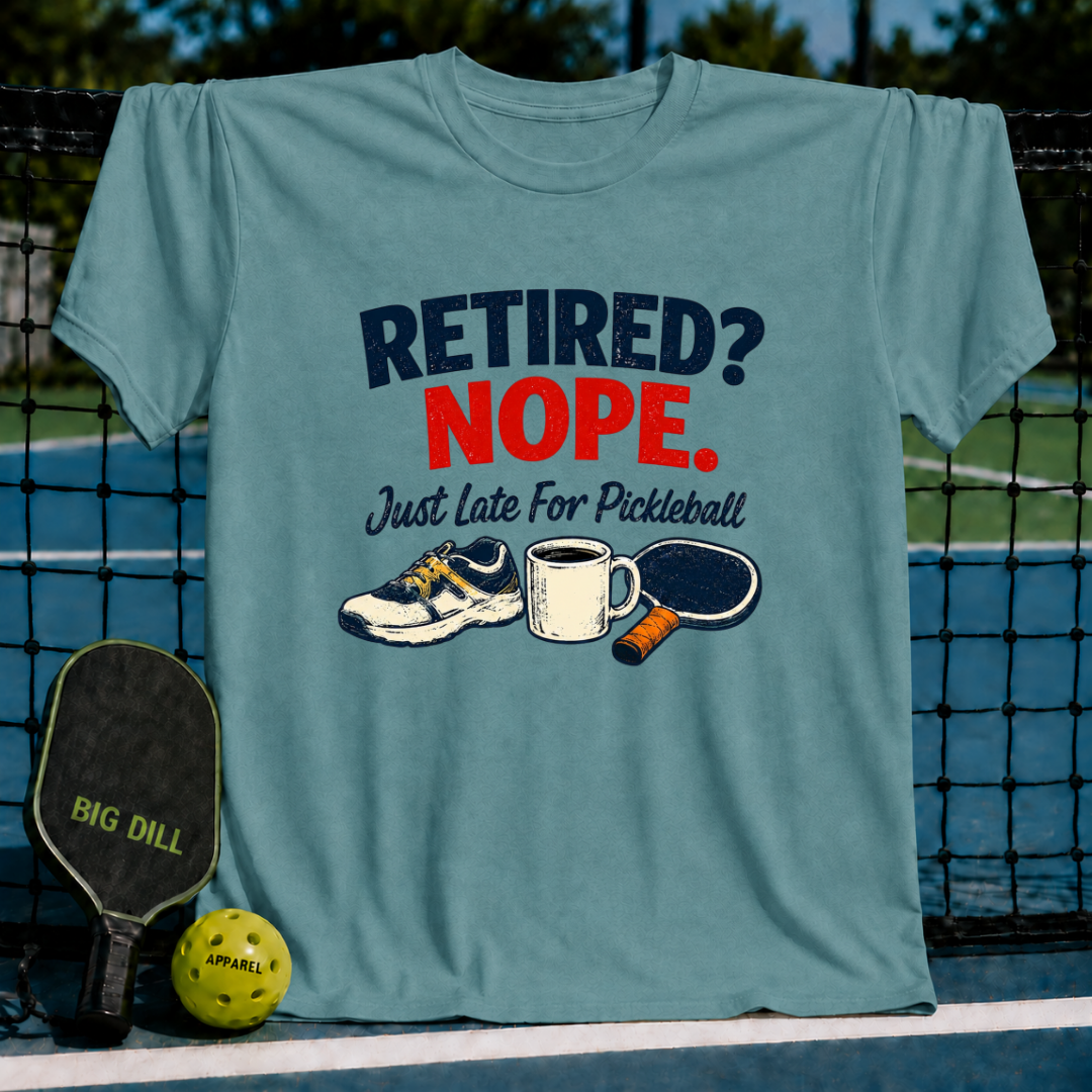 Blue-grey crewneck t-shirt featuring a Retired? Nope. Just Late For Pickleball graphic with a sneaker, coffee mug, and paddle.