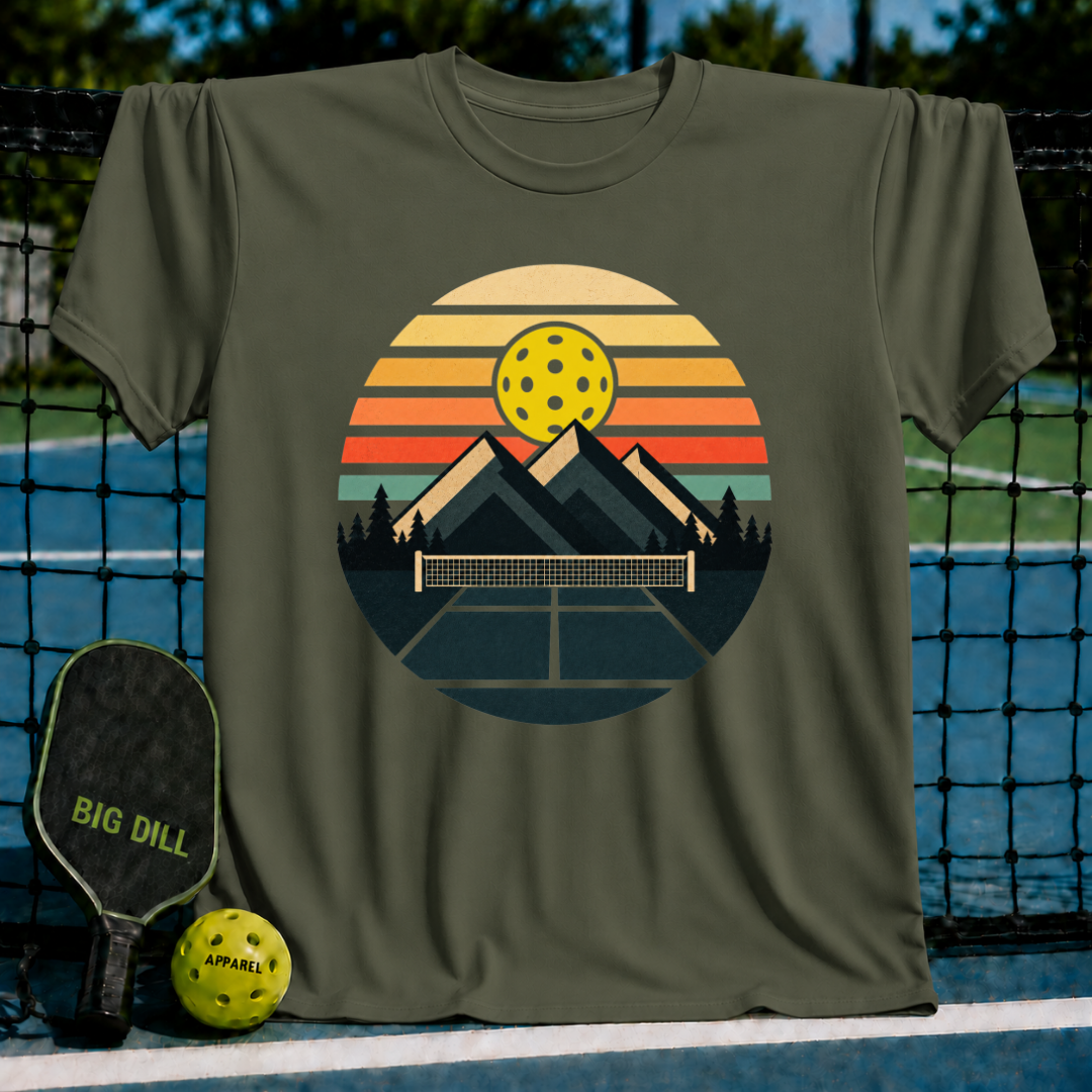Olive green unisex t-shirt featuring a retro circular graphic of mountains, a pickleball net, and a sunset-colored ball.