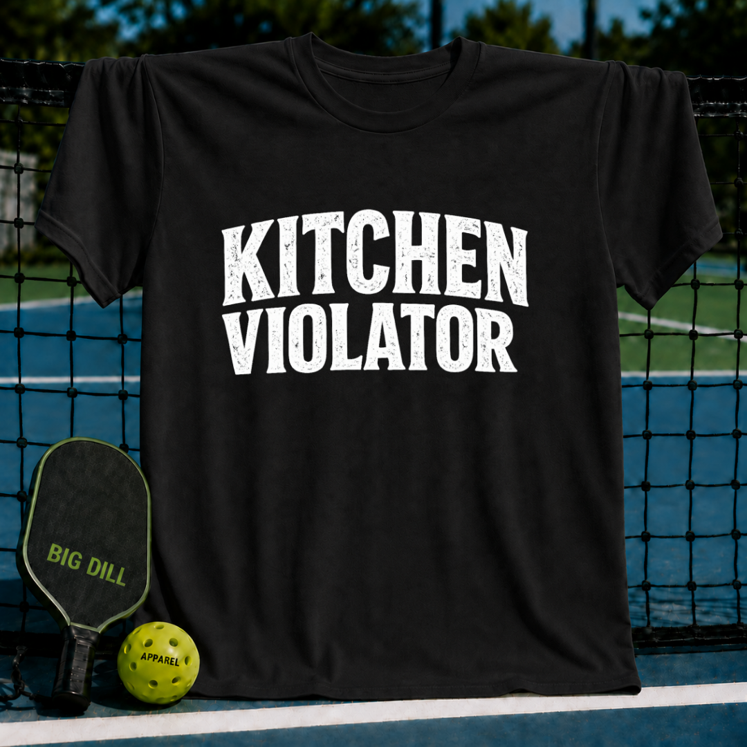 Navy unisex t-shirt featuring distressed white varsity text reading Kitchen Violator, displayed on a pickleball court.
