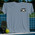 Light blue unisex crewneck t-shirt featuring a small pickleball graphic on the chest, displayed on a pickleball court.