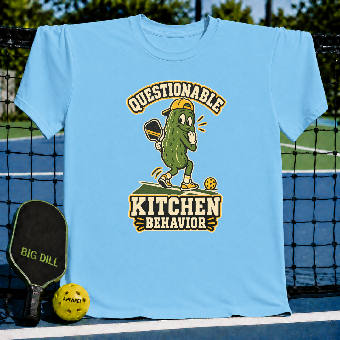 Light blue crew neck t-shirt featuring a cartoon pickle playing pickleball with the text Questionable Kitchen Behavior.