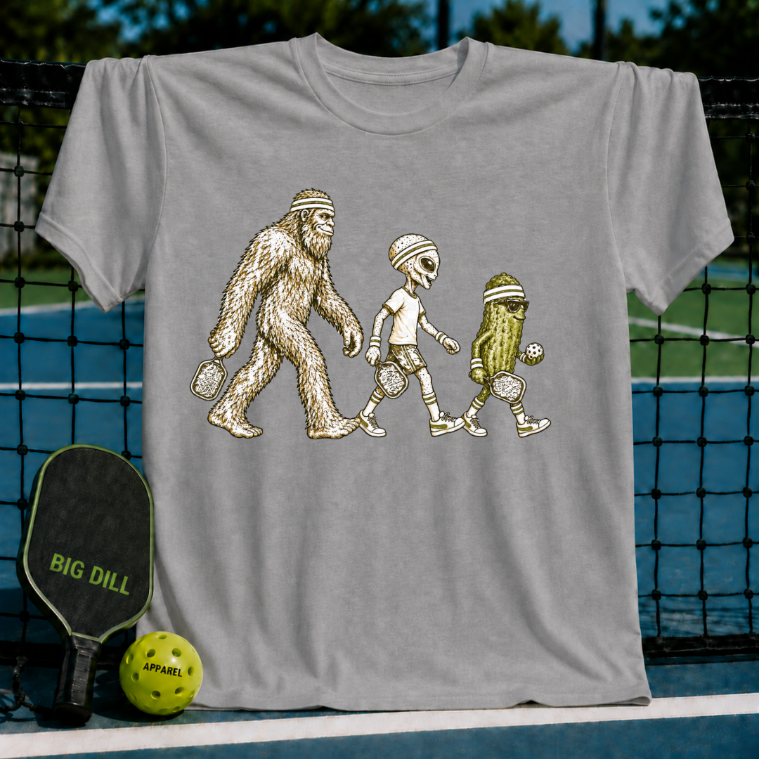 Grey crewneck t-shirt featuring a graphic of Bigfoot, an alien, and a pickle playing pickleball on a court background.