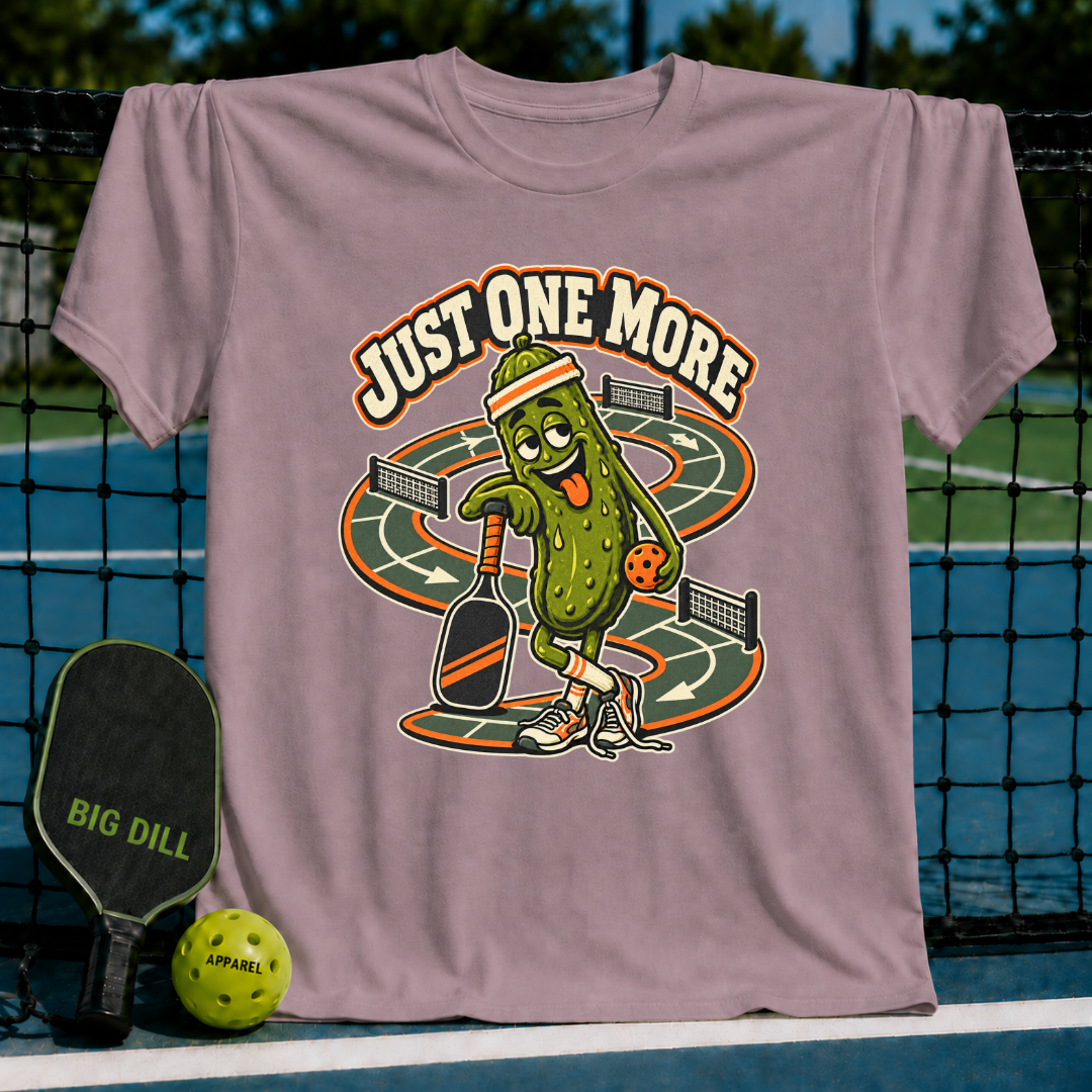 Mauve crewneck t-shirt featuring a cartoon pickle playing pickleball with the text Just One More on a court background.