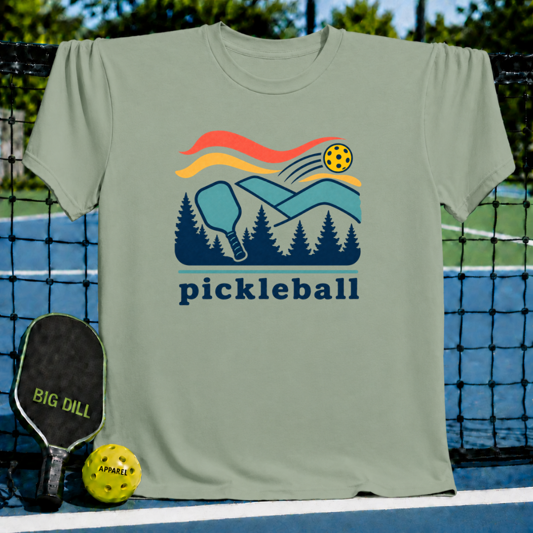 Sage green crewneck t-shirt featuring a retro pickleball, paddle, and forest mountain graphic on a pickleball court.