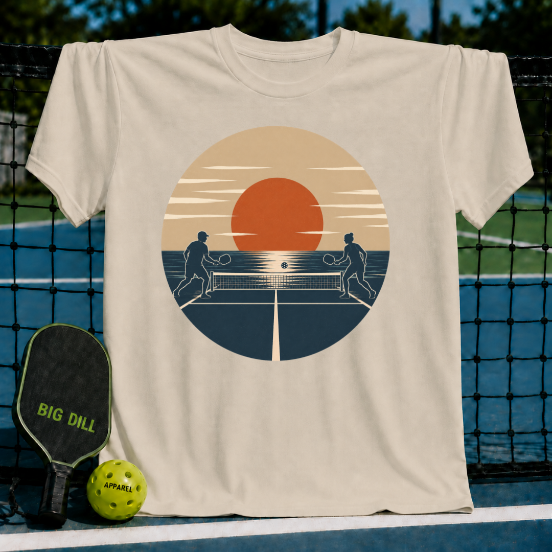 Beige unisex t-shirt featuring a retro sunset graphic of two people playing pickleball on a court.