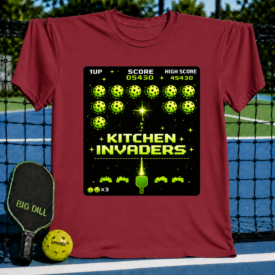 Maroon unisex t-shirt featuring a pixel-art Kitchen Invaders graphic with pickleballs and a paddle on a pickleball court background.
