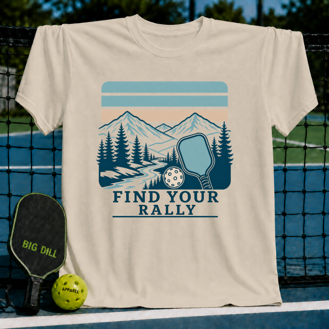 Cream-colored crewneck t-shirt featuring a blue mountain, forest, and pickleball graphic with the text Find Your Rally.