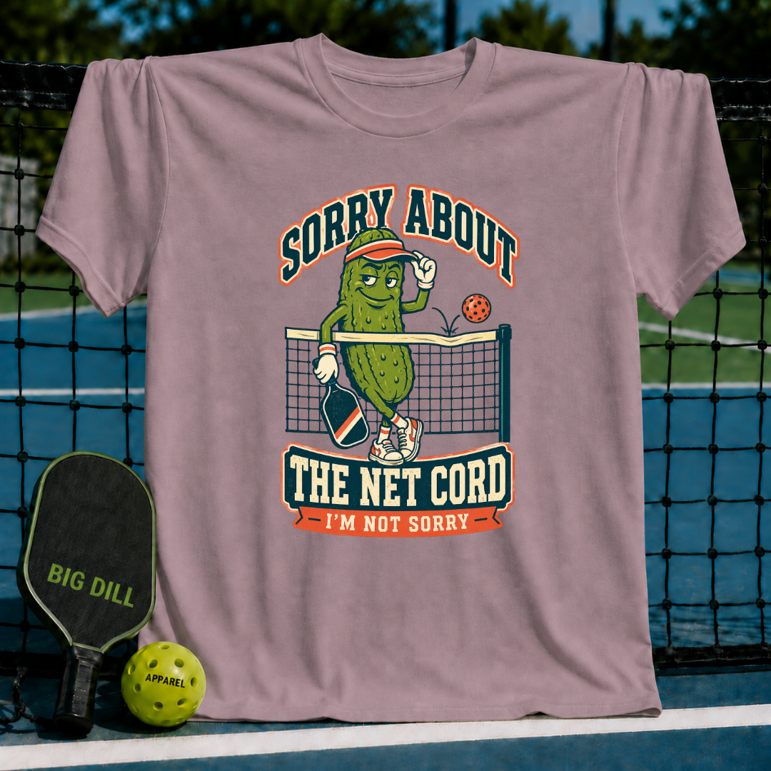 Mauve t-shirt featuring a cartoon pickle playing pickleball with the text Sorry About The Net Cord I'm Not Sorry.
