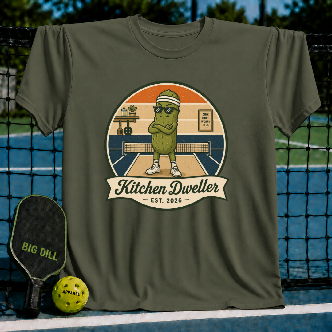 Olive green unisex t-shirt featuring a retro pickle character graphic with sunglasses on a pickleball court.