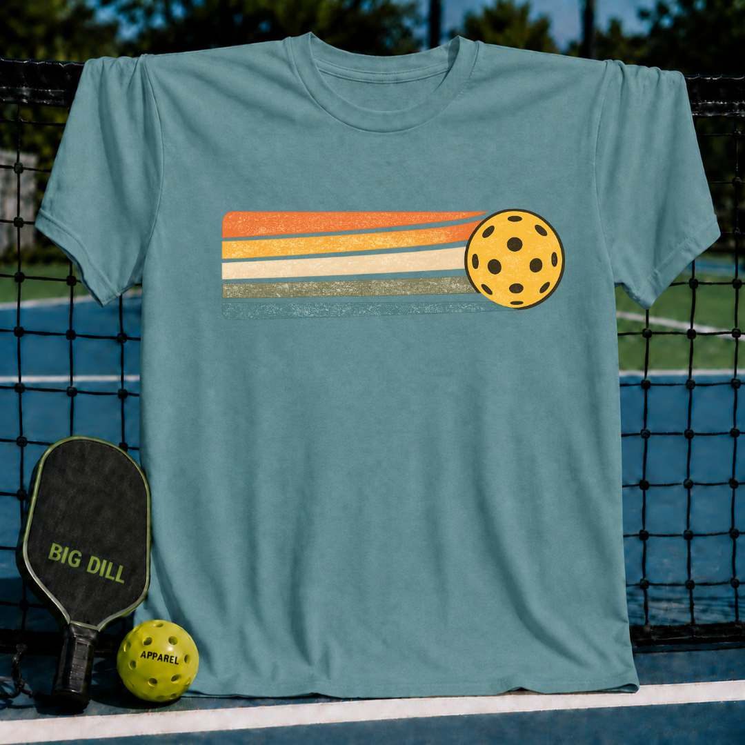 Periwinkle blue unisex t-shirt featuring a yellow pickleball and retro sunset stripes in orange, cream, sage, and teal.