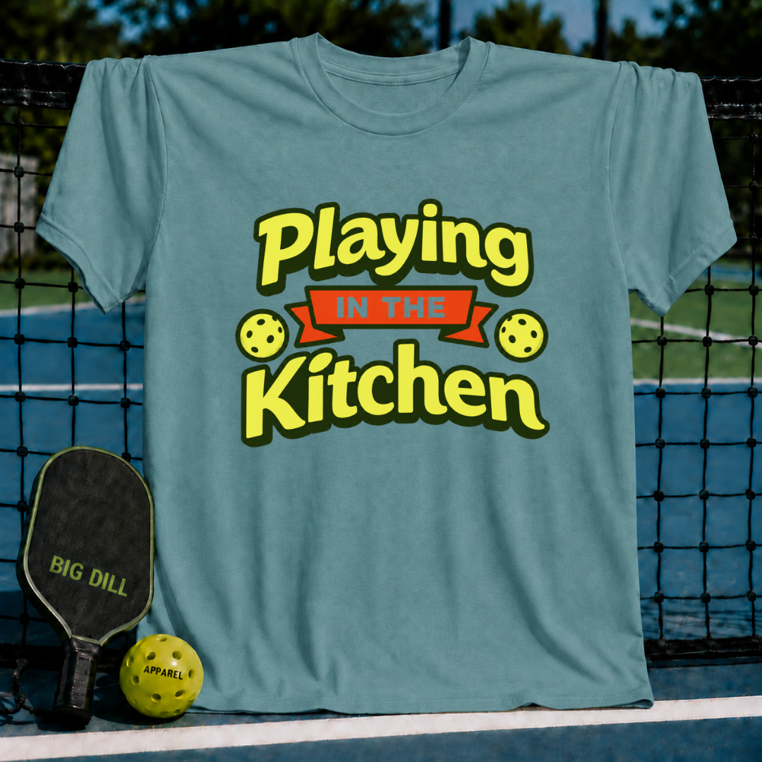 Blue-grey crewneck t-shirt with Playing in the Kitchen text, pickleball graphics, and a paddle on a court background.