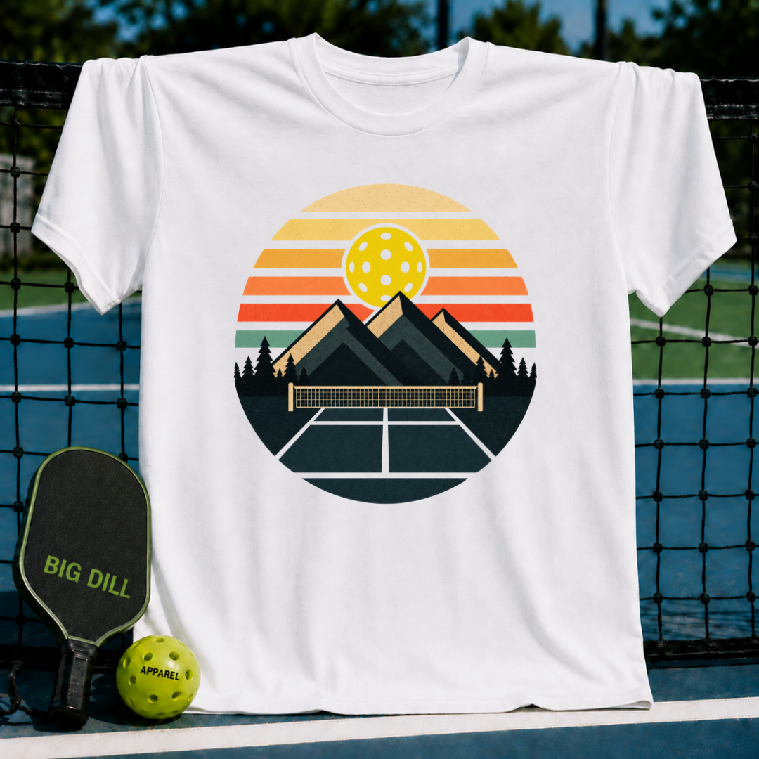 White heavyweight unisex t-shirt featuring a retro circular graphic of mountains, a pickleball net, and a sunset.