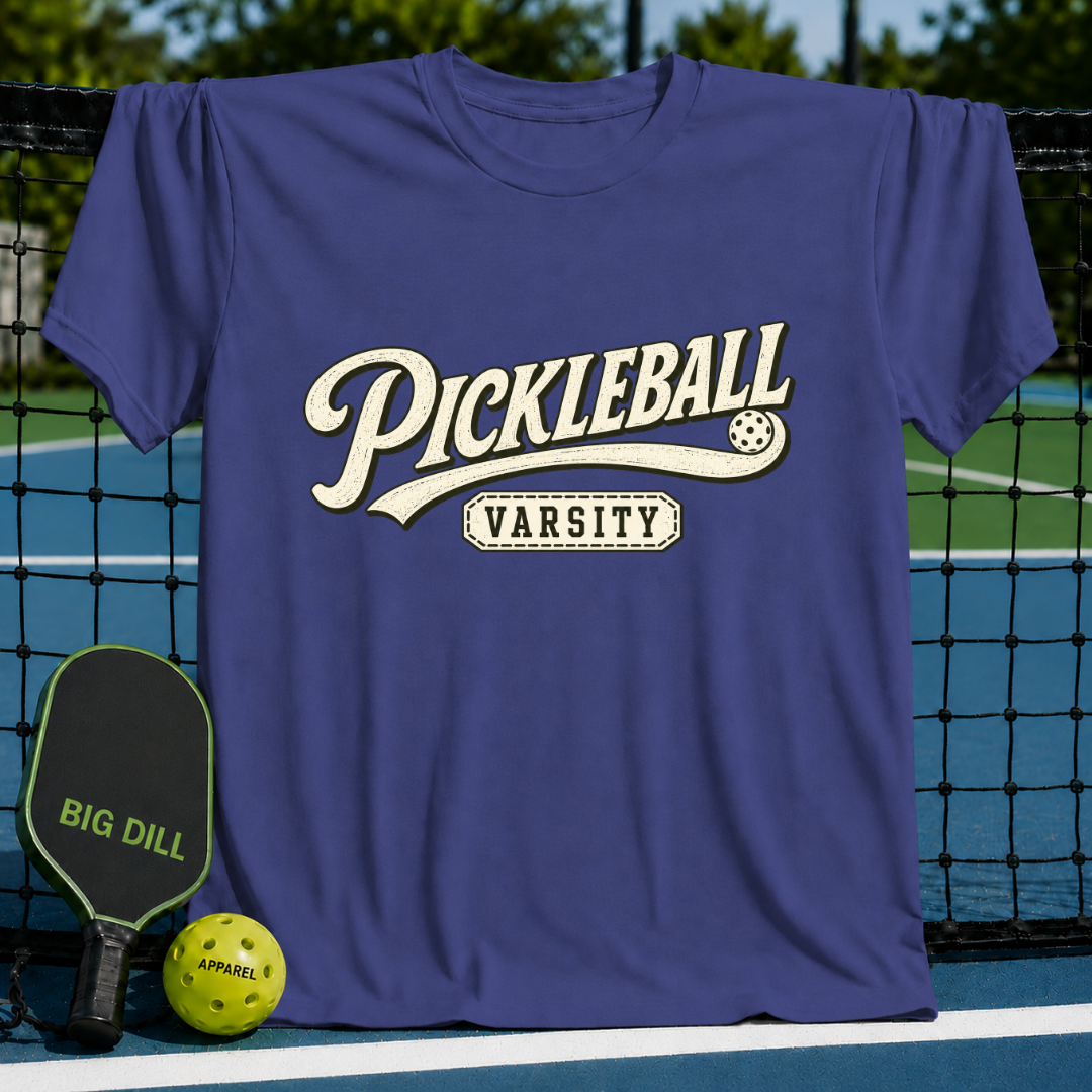 Purple crewneck t-shirt featuring vintage-style Pickleball Varsity graphic, displayed on a pickleball court net.