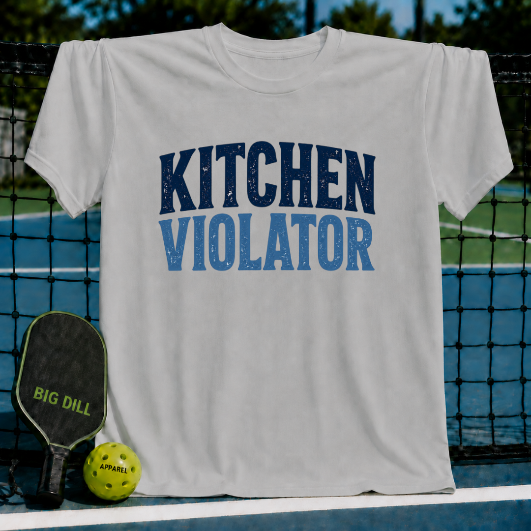 Light gray unisex t-shirt featuring distressed blue Kitchen Violator varsity lettering, displayed on a pickleball court.