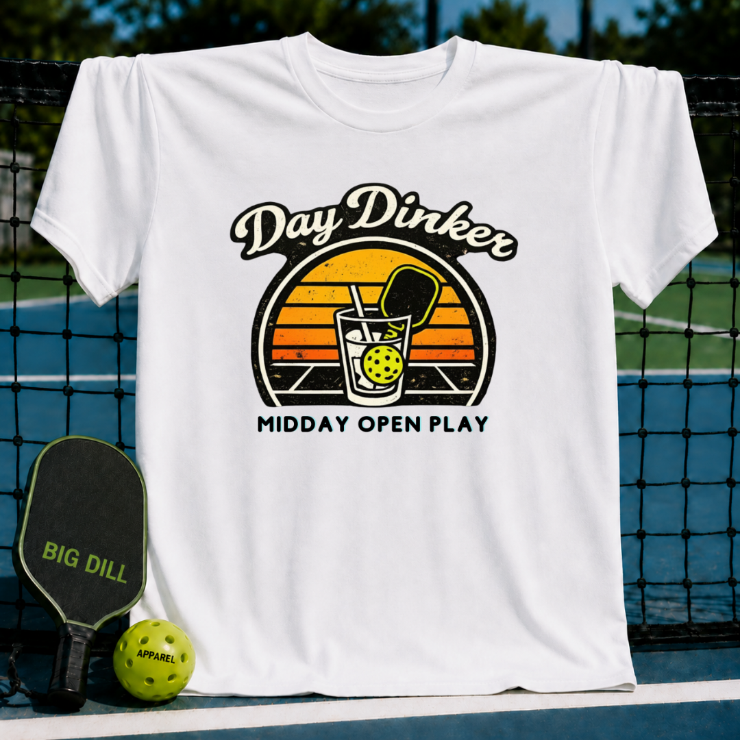 White unisex T-shirt featuring a retro sunset graphic with a pickleball paddle and ball in a glass, set on a court.