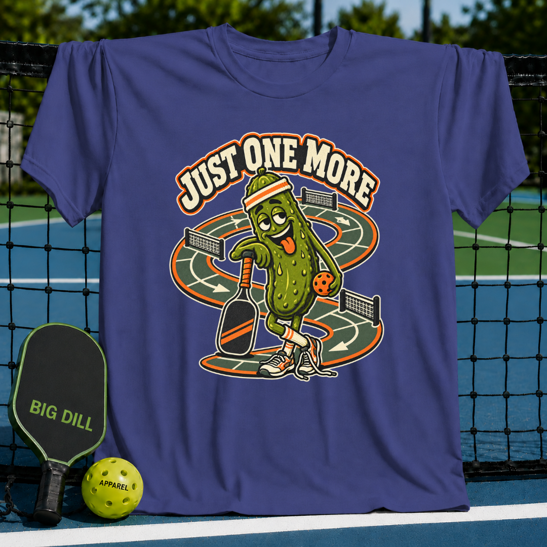 Purple cotton t-shirt featuring a cartoon pickle playing pickleball with the text Just One More on a pickleball court background.