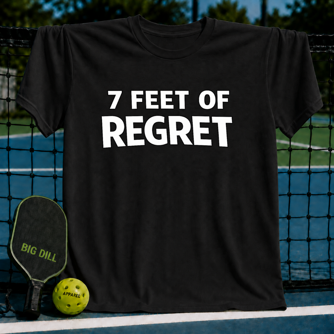 Black unisex t-shirt featuring bold white text reading 7 FEET OF REGRET, displayed on a pickleball court with a paddle and ball.