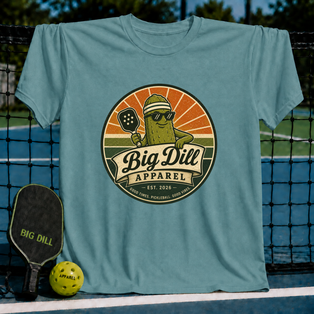 Blue-green unisex pickleball t-shirt featuring a retro circular badge graphic of a pickle mascot with a paddle and sunglasses.