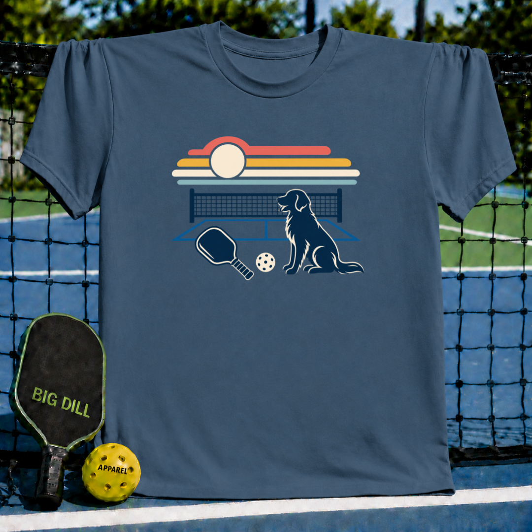 Blue crewneck t-shirt featuring a retro sunset, dog, pickleball paddle, and ball graphic on a pickleball court background.