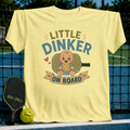 Light yellow maternity t-shirt featuring a Little Dinker On Board graphic with a baby holding a pickleball on a court.