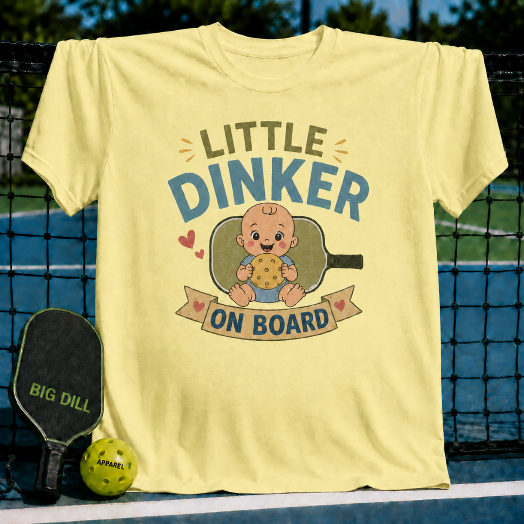Light yellow maternity t-shirt featuring a Little Dinker On Board graphic with a baby holding a pickleball on a court.