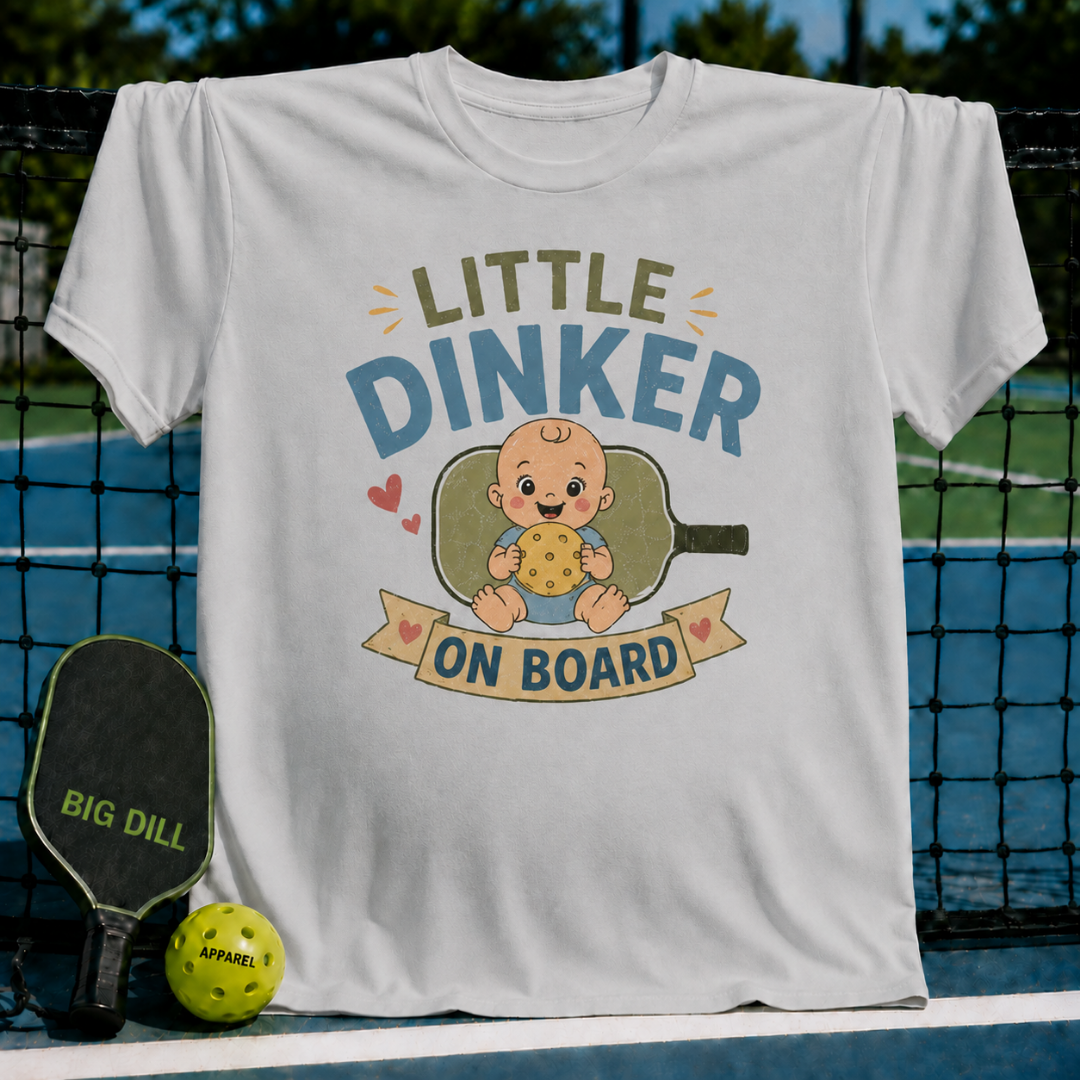White unisex maternity t-shirt featuring a Little Dinker On Board graphic with a baby holding a pickleball on a court.