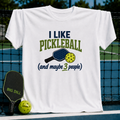 White unisex t-shirt featuring collegiate-style text, a pickleball paddle, and ball graphic on a pickleball court background.