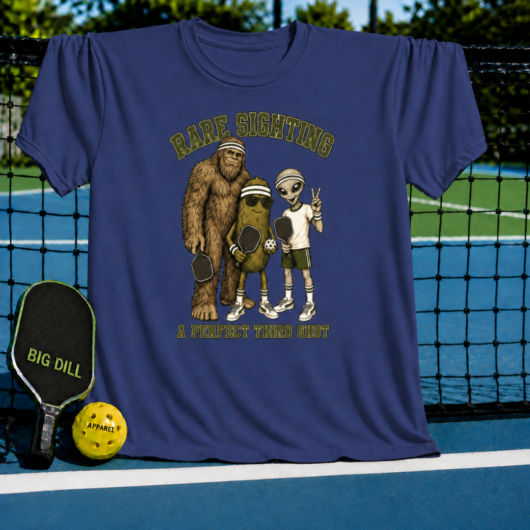 Navy blue T-shirt featuring a Bigfoot, pickle, and alien playing pickleball with Rare Sighting text on a court background.