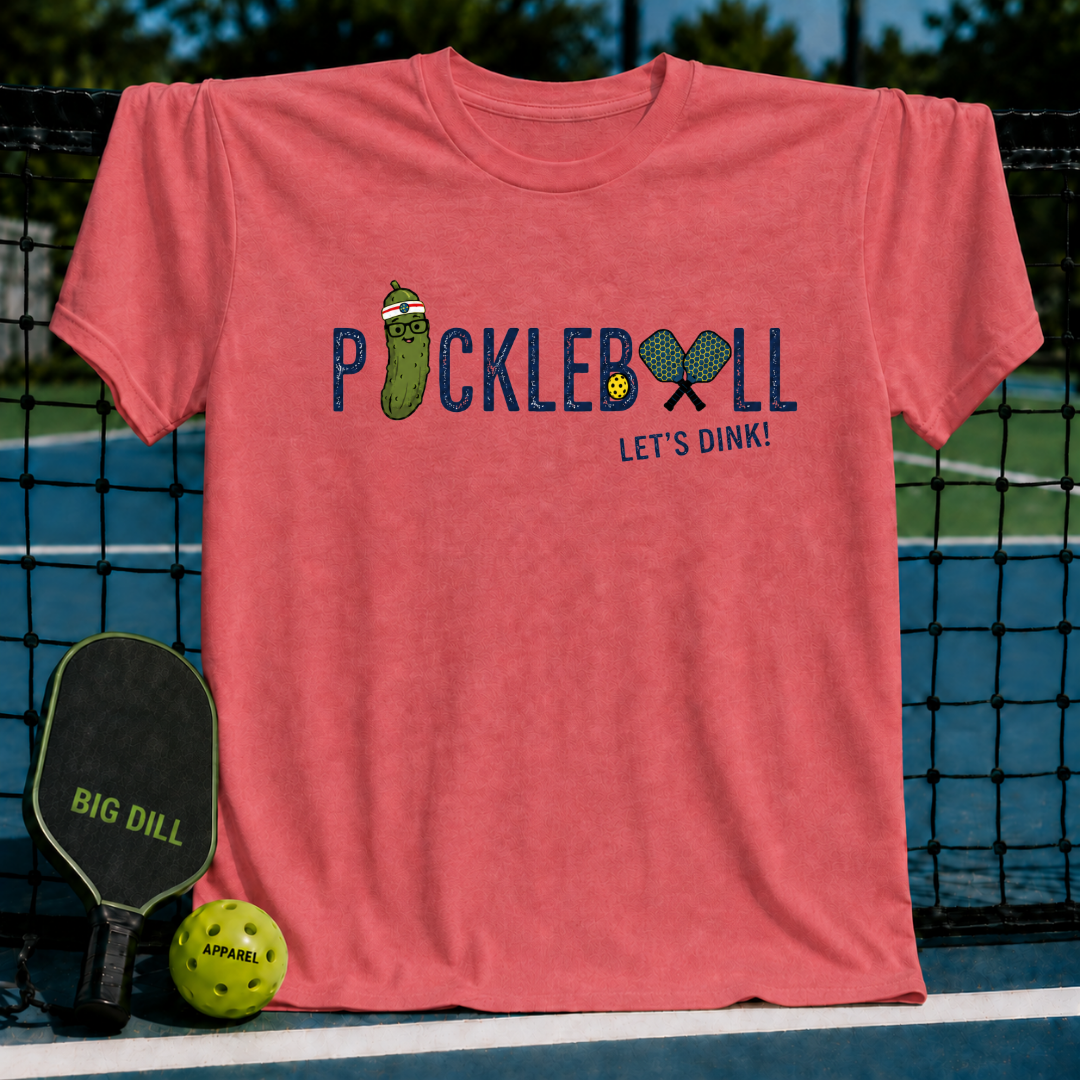 Coral red crewneck t-shirt featuring a Pickleball Let's Dink graphic with a pickle character and paddles on a court.