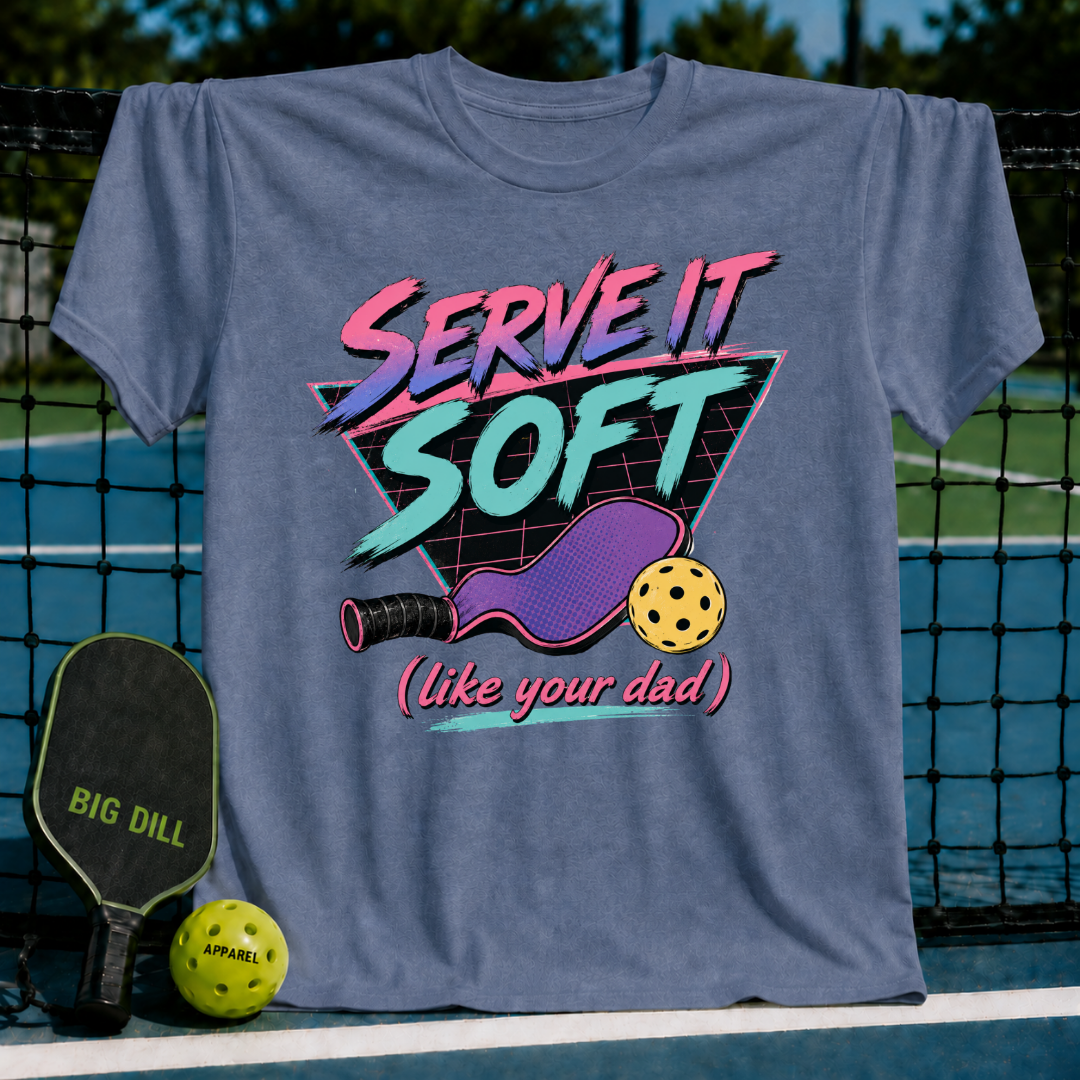 Slate blue unisex t-shirt featuring a retro 80s neon graphic of a pickleball paddle and ball with Serve It Soft text.