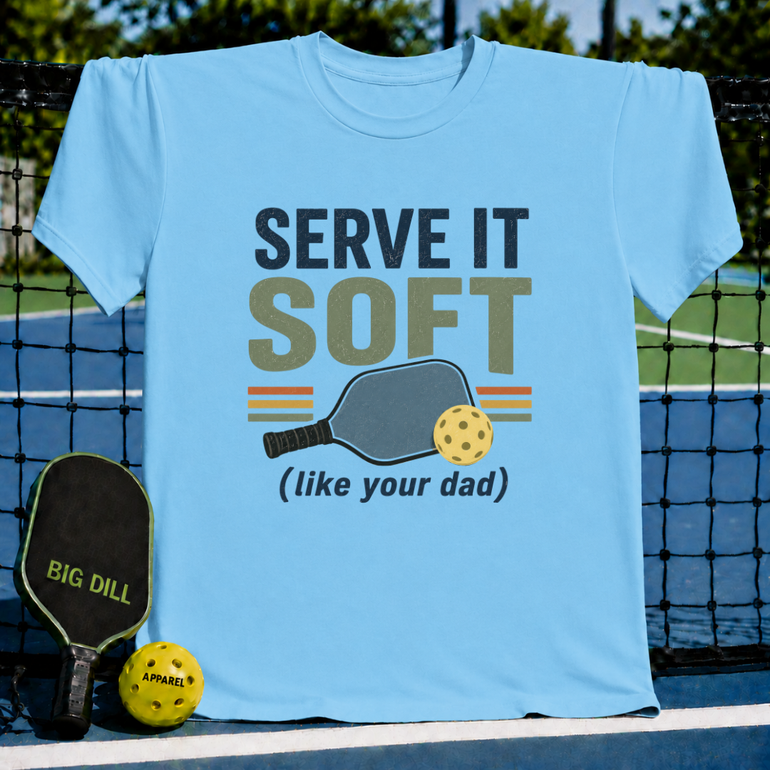 Light blue unisex t-shirt featuring retro Serve It Soft pickleball typography, paddle, and ball graphic on a court.