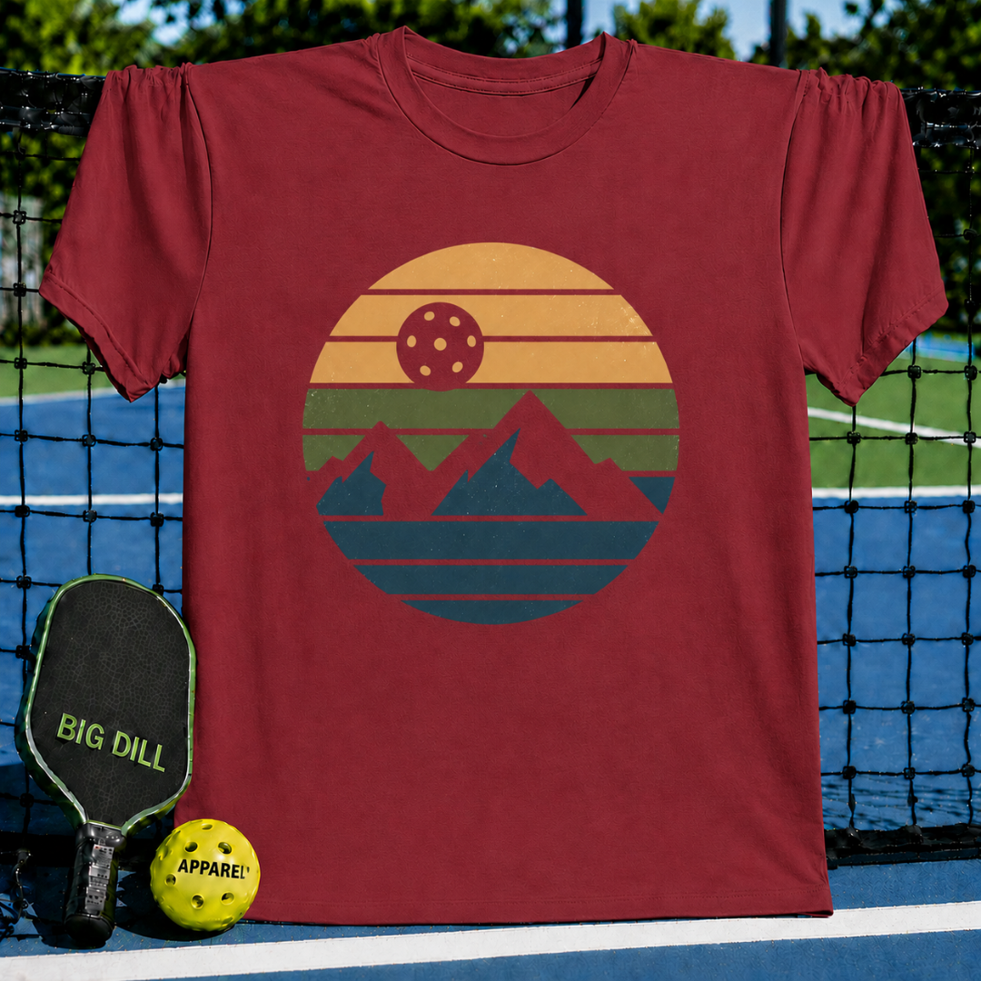 Maroon unisex t-shirt featuring a retro circular graphic of mountains and a pickleball sun on a pickleball court.