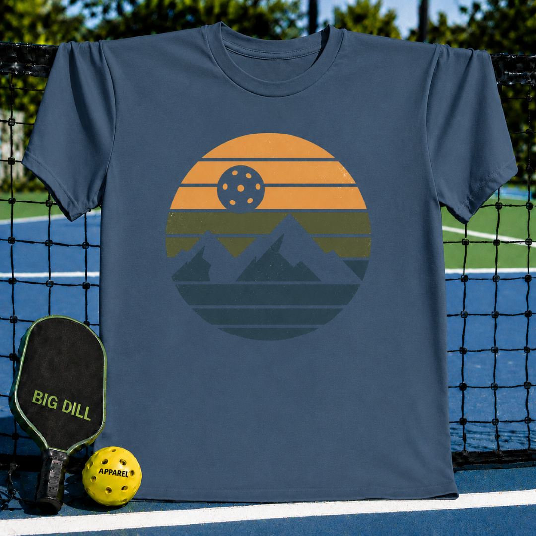 Blue unisex t-shirt featuring a retro circular graphic of mountains and a pickleball sun on a pickleball court.