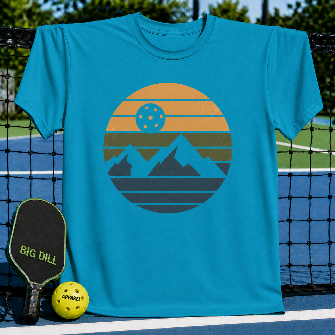 Mint green unisex t-shirt featuring a retro circular graphic of mountains and a pickleball sun on a pickleball court.