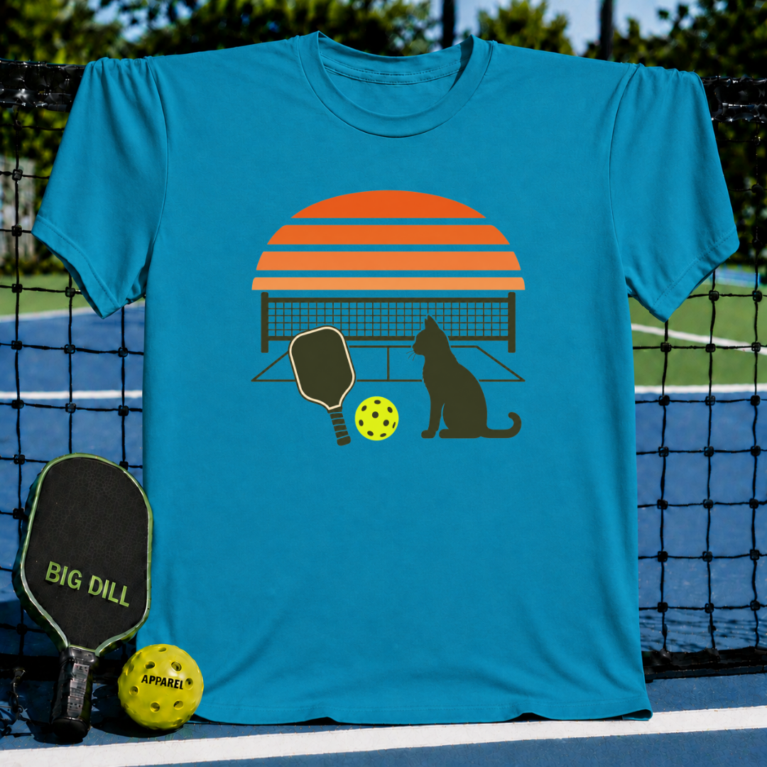 Blue unisex t-shirt featuring a retro sunset, pickleball court, paddle, ball, and cat silhouette graphic.