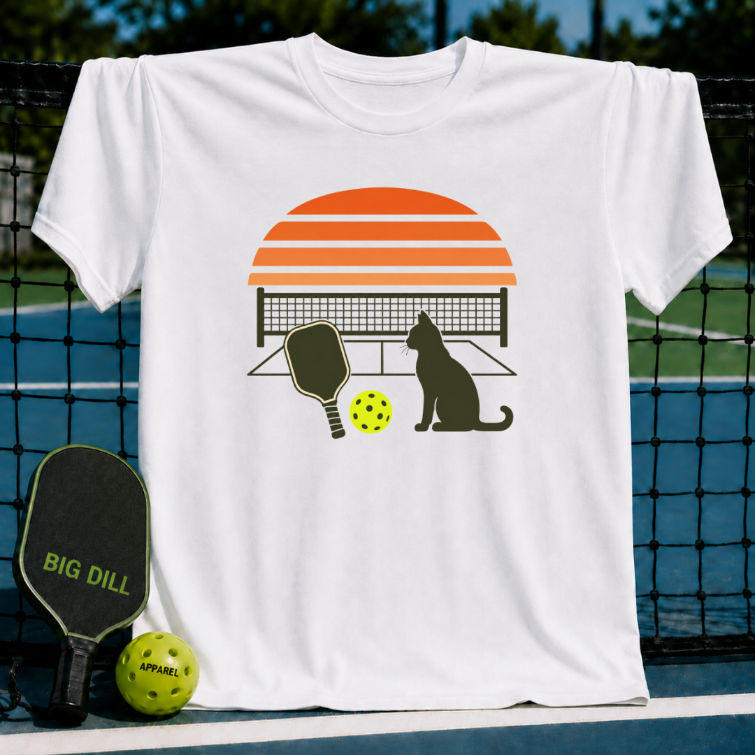White unisex t-shirt featuring a retro orange sunset, cat silhouette, pickleball paddle, and ball graphic.