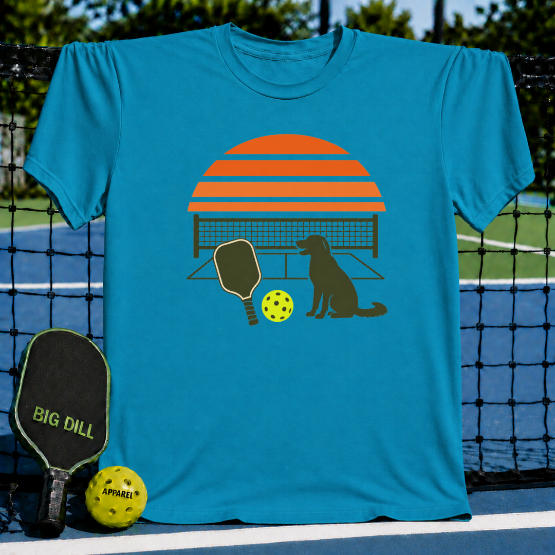 Bright blue crewneck t-shirt featuring a retro orange sunset, pickleball paddle, ball, and dog silhouette graphic.