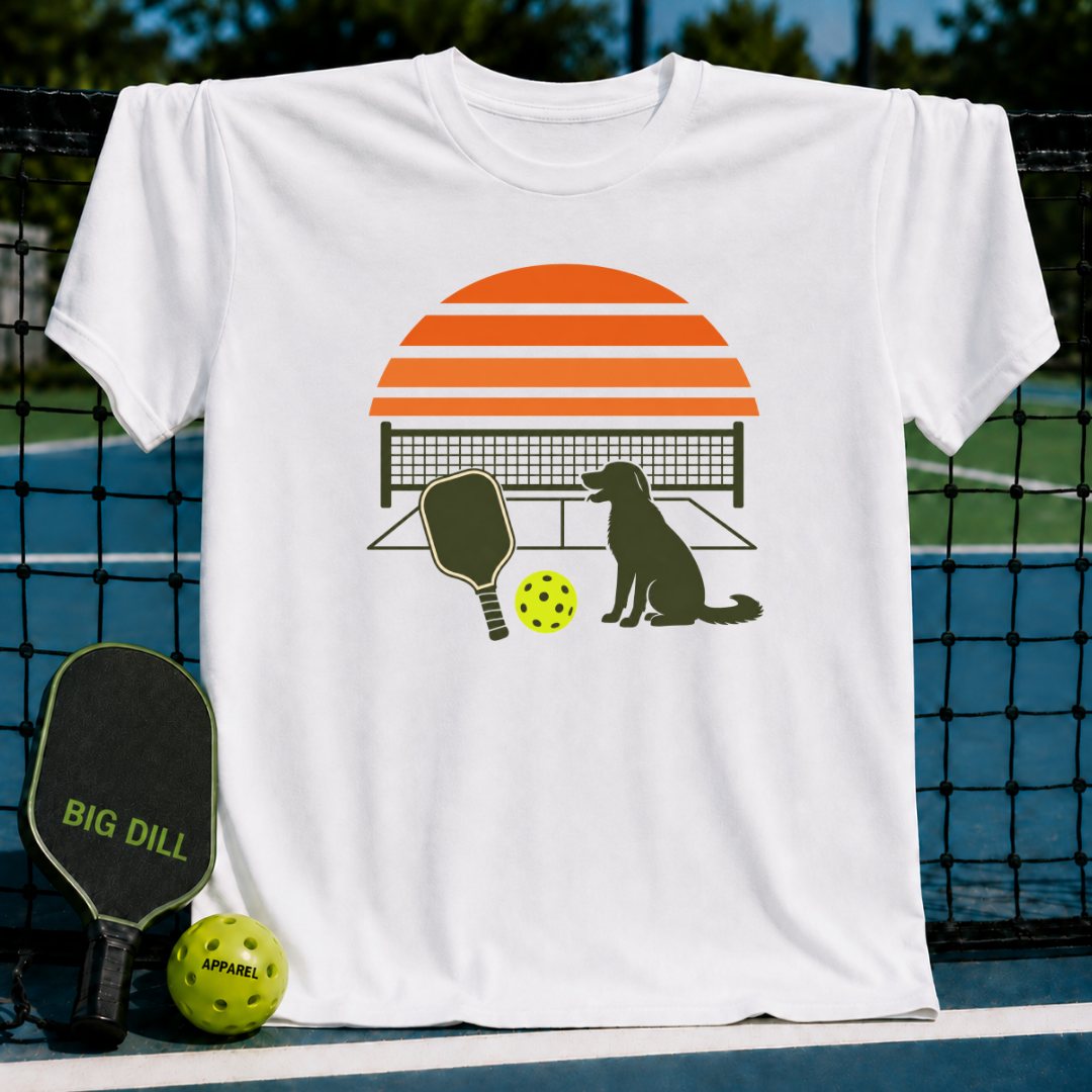 White crew neck t-shirt featuring a retro orange sunset, pickleball court, paddle, and dog graphic on a pickleball court.