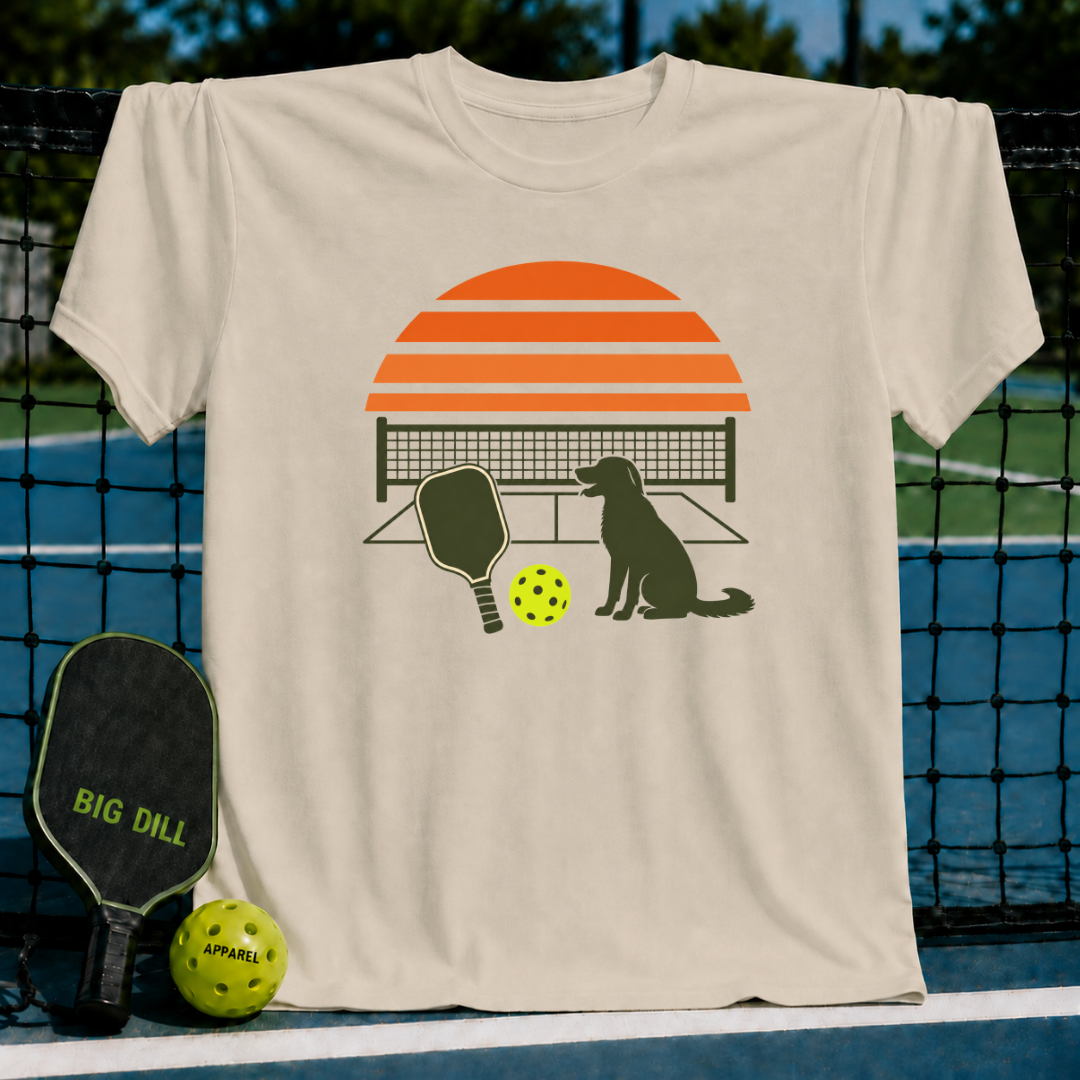 Beige crew neck t-shirt featuring a retro orange sunset, pickleball court, paddle, and dog graphic.