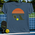 Blue crewneck t-shirt featuring a retro orange sunset, pickleball paddle, ball, and dog silhouette graphic.