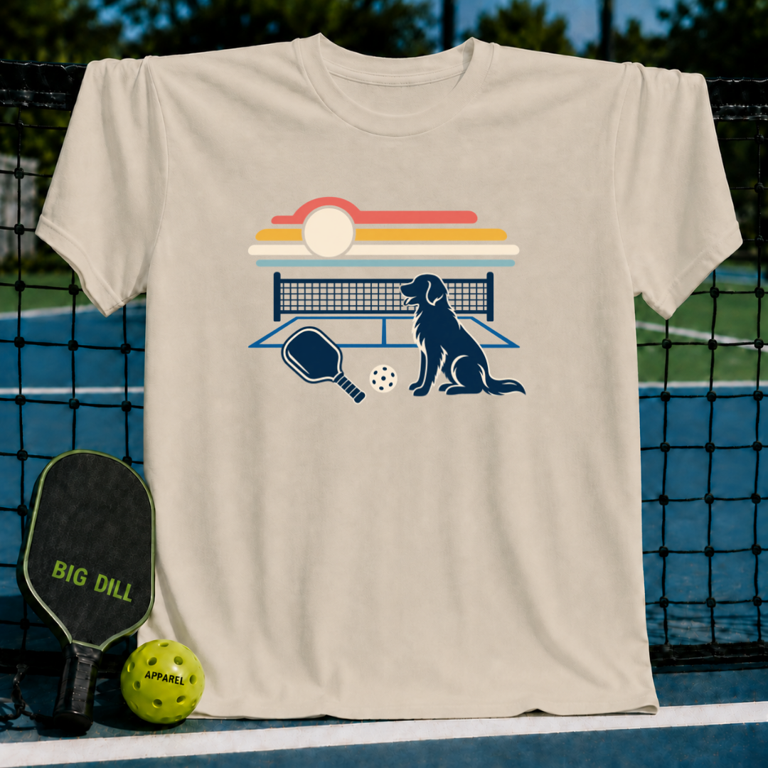 Beige cotton t-shirt featuring a retro sunset, pickleball court, paddle, and dog graphic on a pickleball court background.