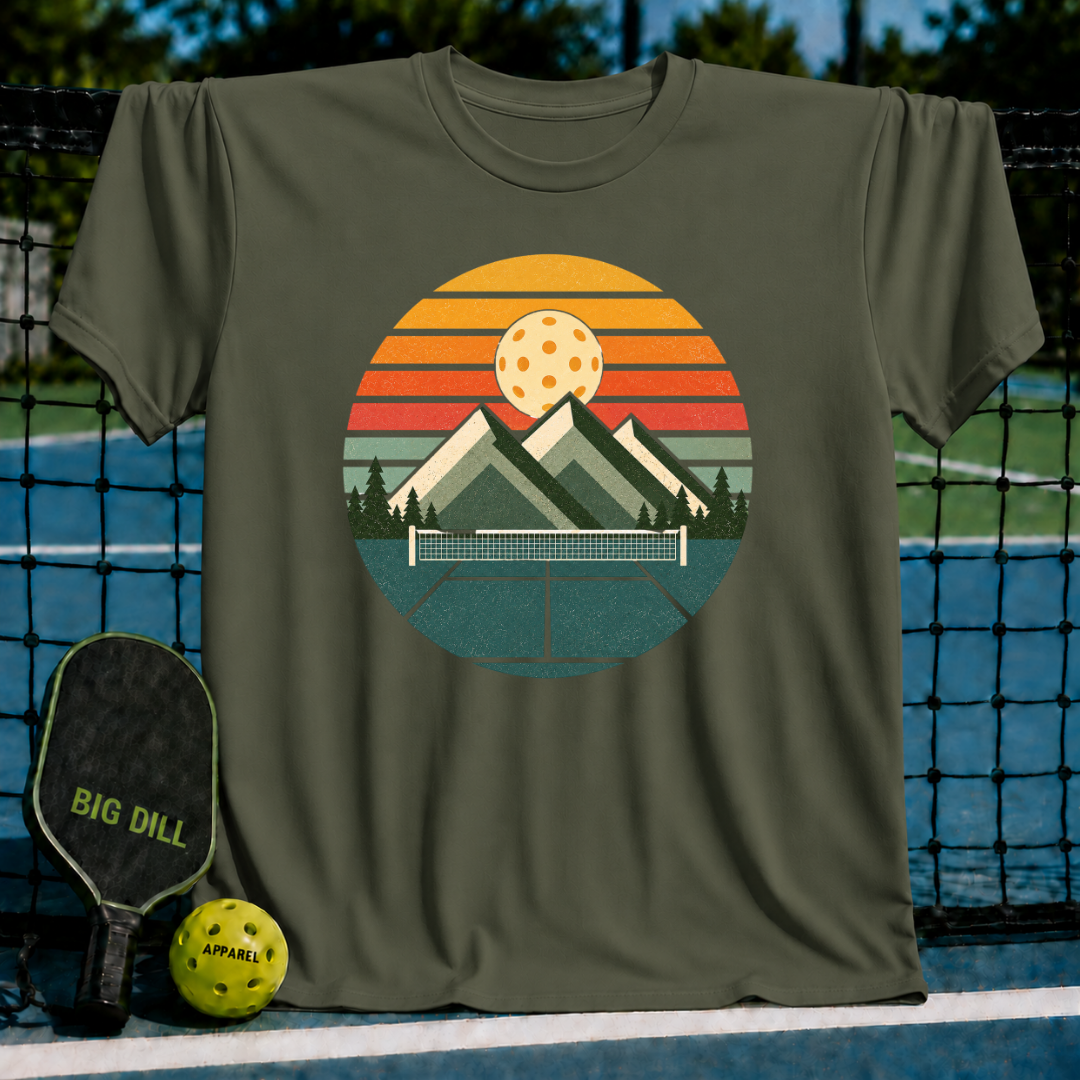 Deep teal unisex t-shirt featuring a retro circular graphic of mountains, a pickleball net, and a sunset-colored ball.